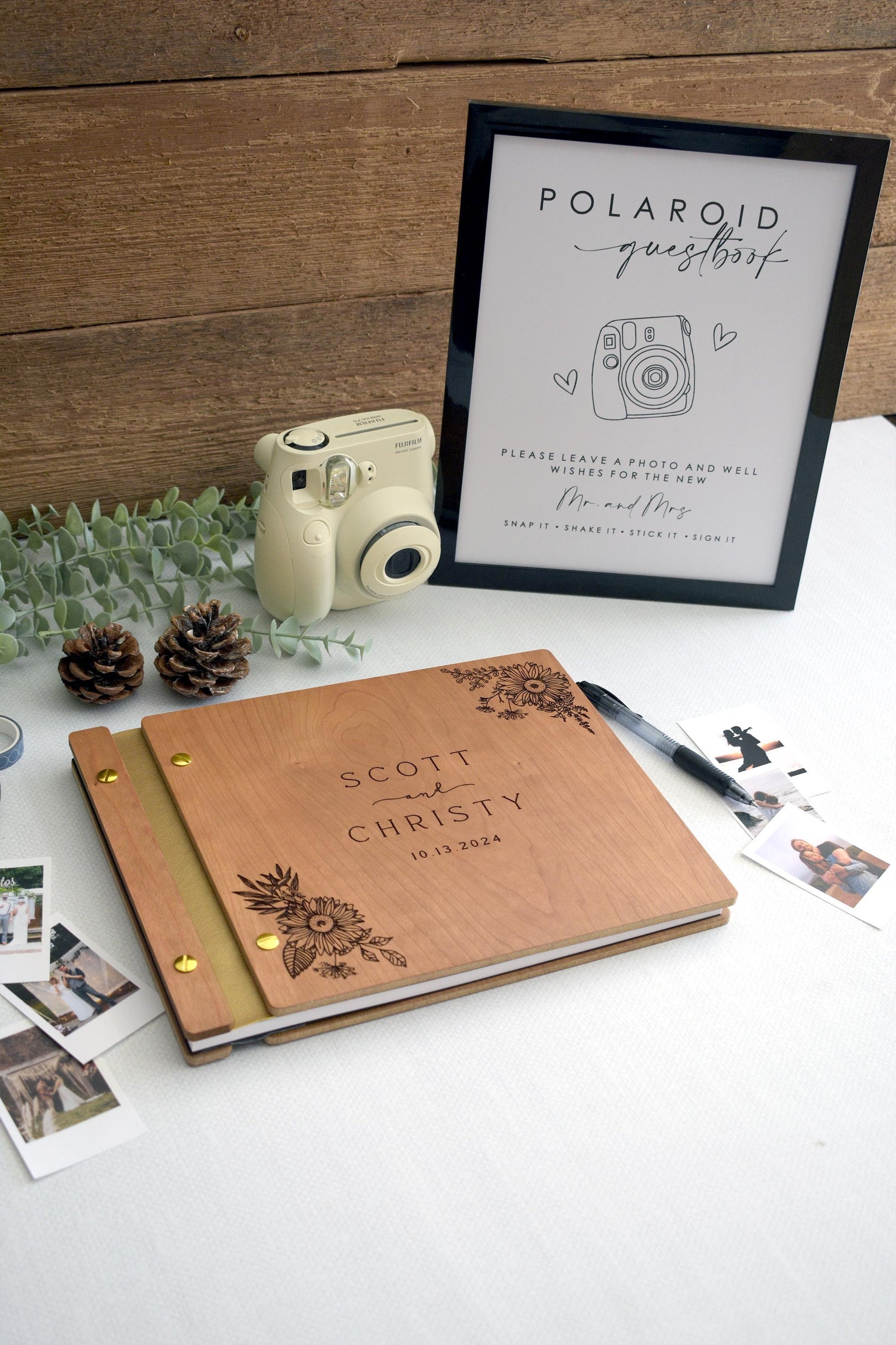 Custom cherry wood wedding guest book with an engraved floral sunflower design. Gold screws and gold leather binding. Surrounded by Polaroid photos, a pen, and photo tape, perfect for capturing special memories at weddings and significant events