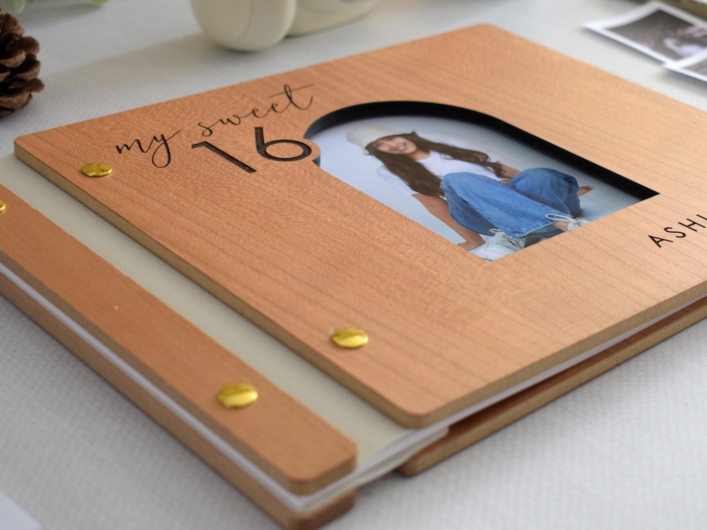 Custom wooden Sweet 16 guest book with a personalized photo and name engraving. Features a cherry wood cover, gold screws, and my sweet 16 design. Ideal for capturing special memories and messages. Surrounded by Polaroid photos and stationery.