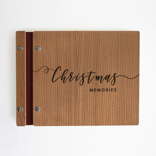 An 8.5x11" guest book lies on a table. Made of cherry wood, burgundy vegan leather binding, and silver hardware. The front cover reads Christmas Memories.