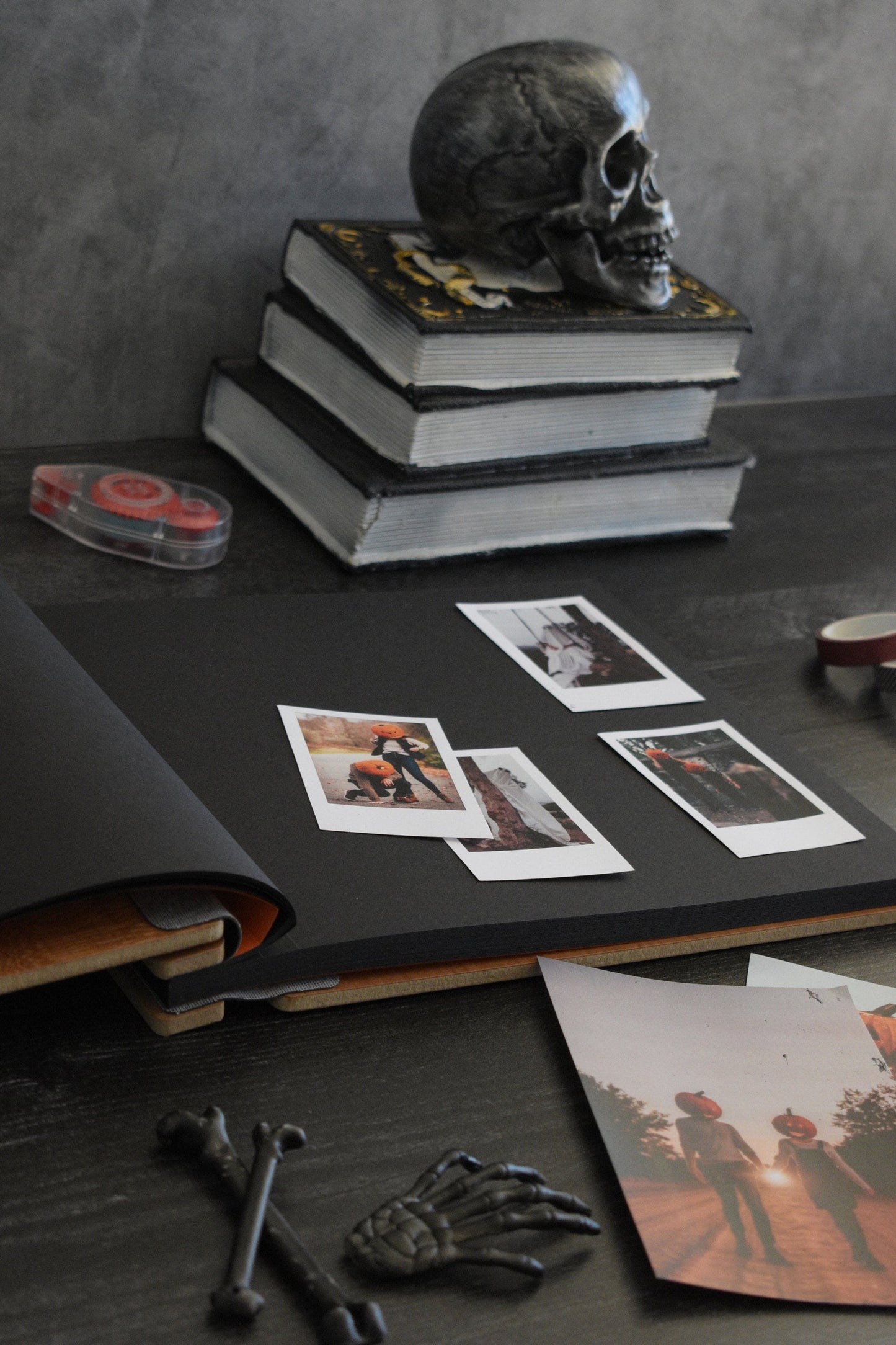 An 8.5x11" guest book lies open on a table with black cardstock pages. Polaroid pictures lay on top of the pages wth halloween decor such as pumpkins and skeletons.