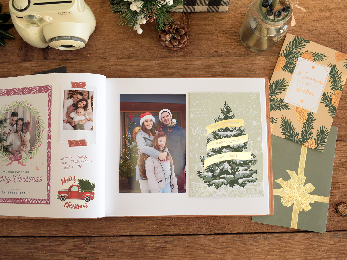 a family photo album with a family photo of a man, woman, and child, along with a Christmas card and a gift box on a wooden surface.