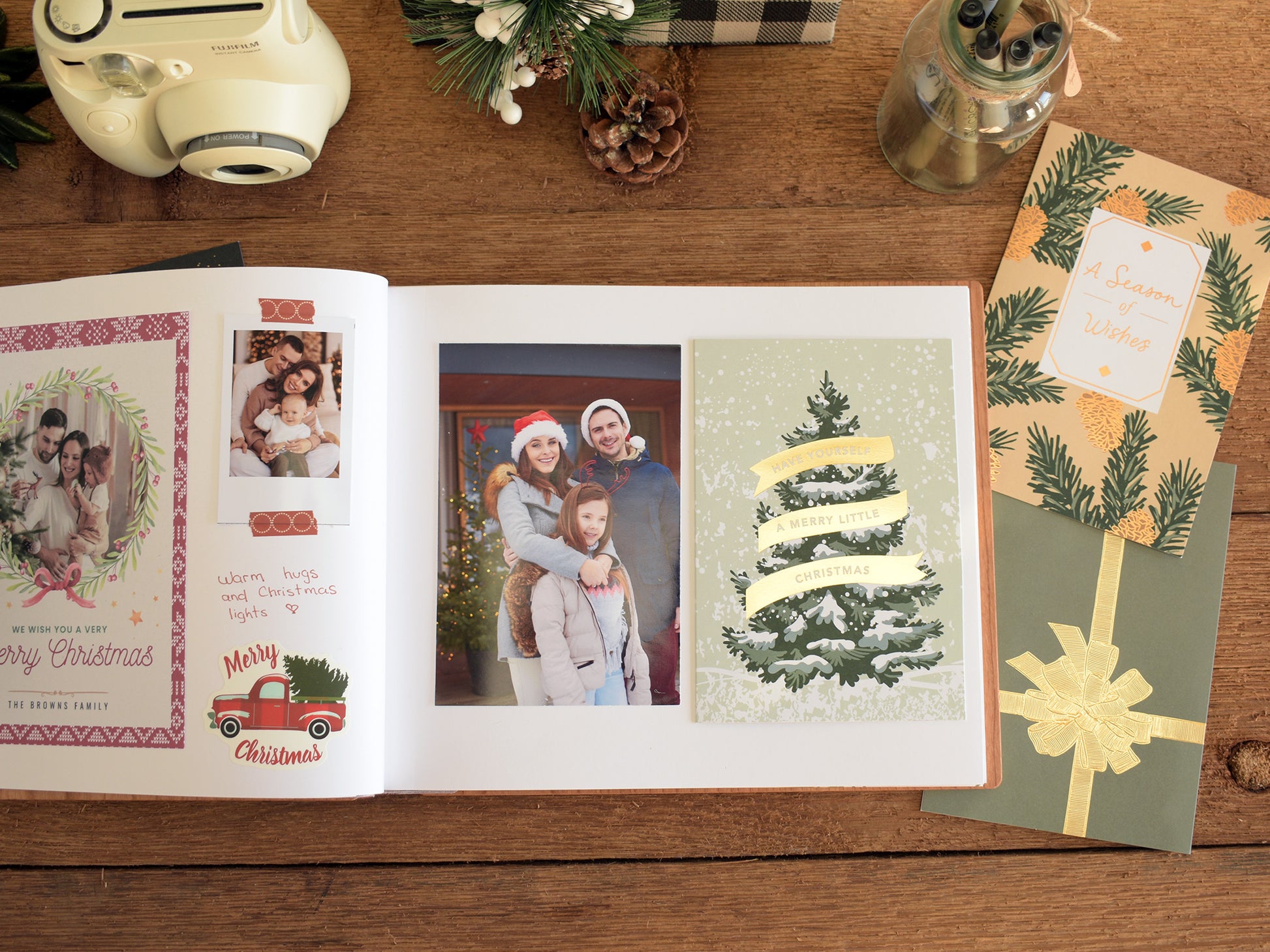 a family photo album with a family photo of a man, woman, and child, along with a Christmas card and a gift box on a wooden surface.