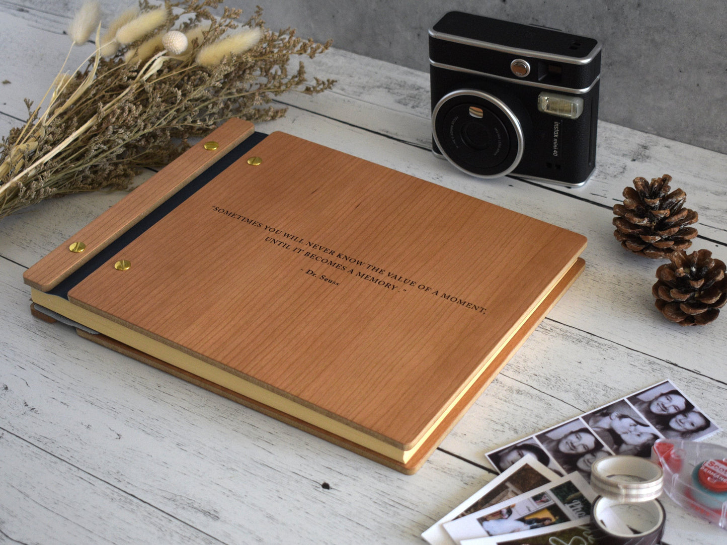 An angled view of a large-sized scrapbook with a retro camera and floral sit beside it. Photo booth strips lie next to the book with washi tape and chestnuts.