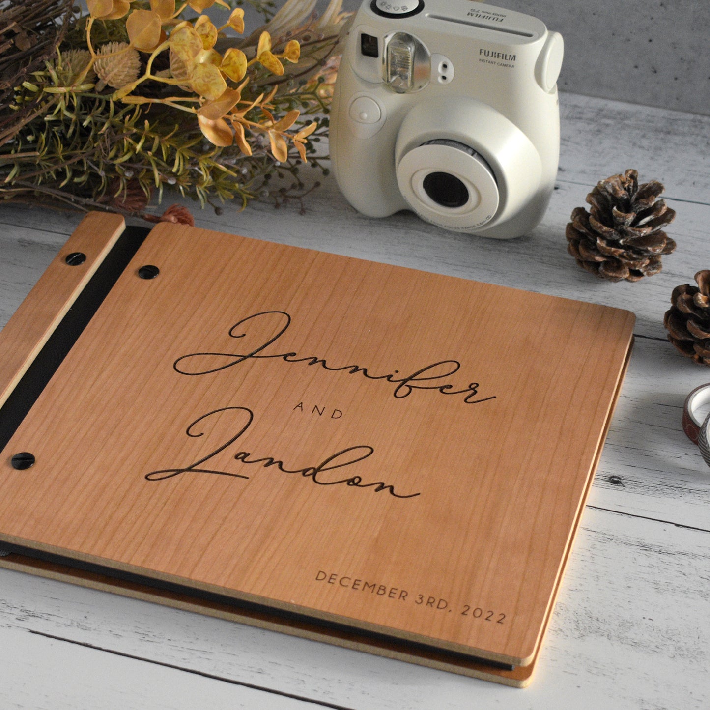 An 8.5x11" guest book lies on a table. Made of cherry wood, black vegan leather binding, and copper hardware. The front cover reads “Jonathan and Christina, January 1, 2023.” 