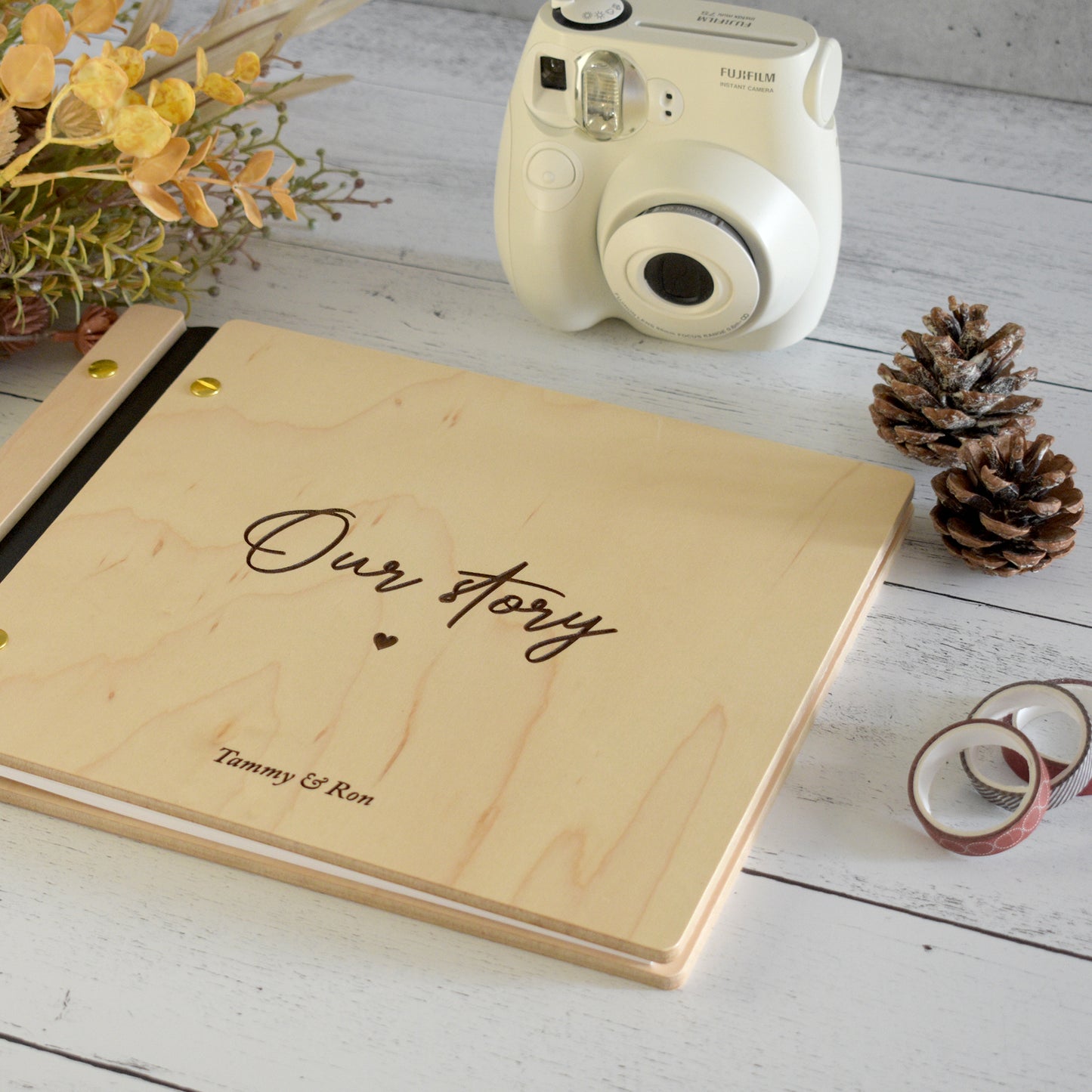 An 8.5x11" guest book lies on a table. Made of maple wood, black vegan leather binding, and gold hardware. The front cover reads “Our Story, Ron & Tammy.”