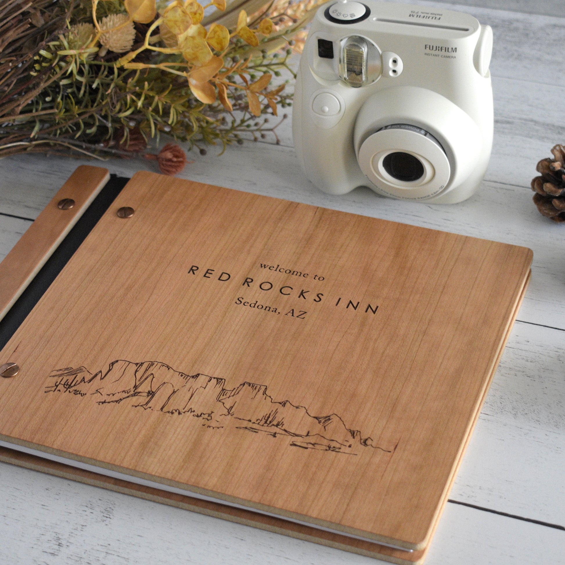 An 8.5x11" Airbnb guest book lies on a table. Made of cherry wood, black vegan leather binding, and copper hardware. The front cover reads Welcome to Red Rocks Inn, Sedona, AZ.