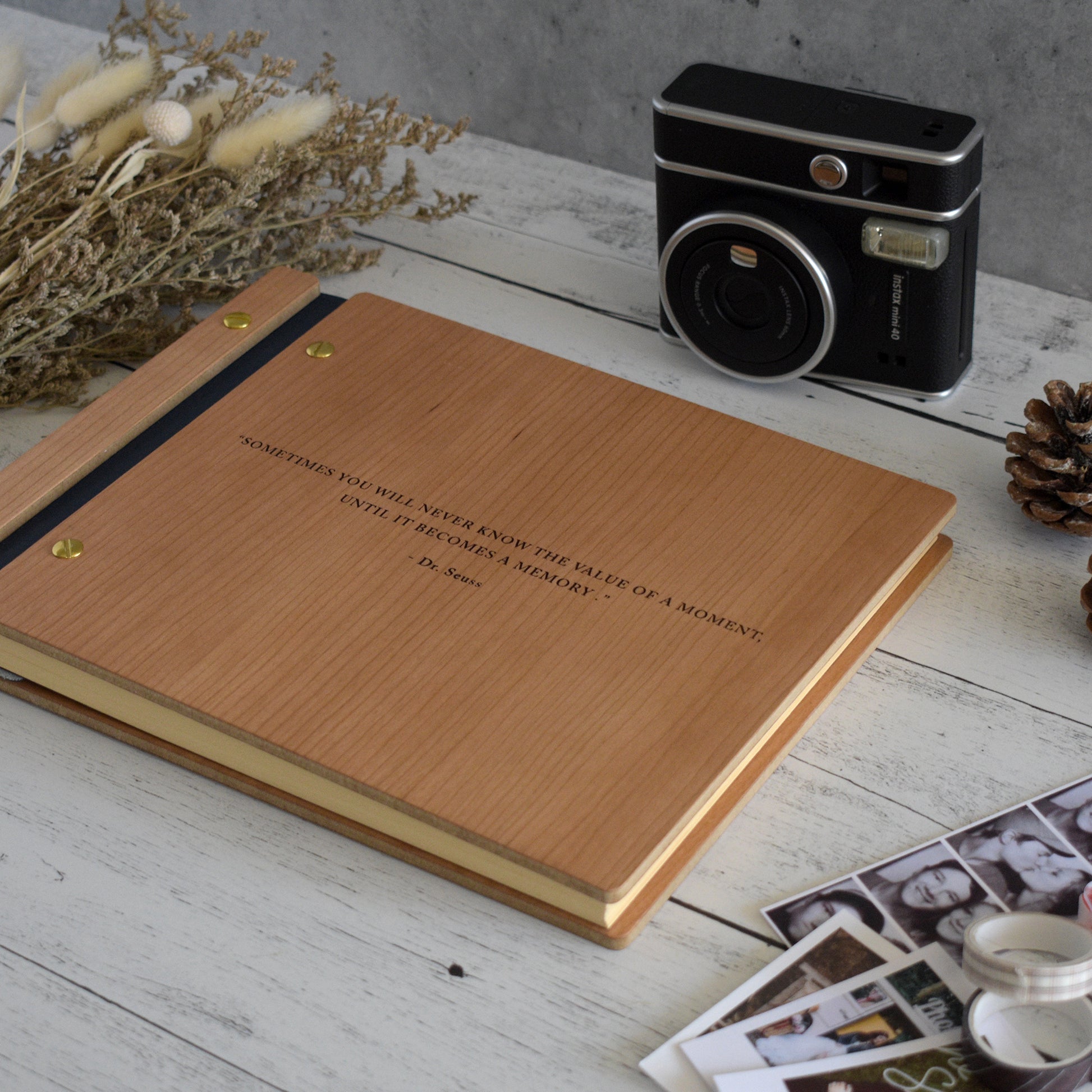 An 8.5x11" guest book lies on a table. Made of cherry wood, navy vegan leather binding, and gold hardware. The front cover includes an engraved design with a personalized quote.