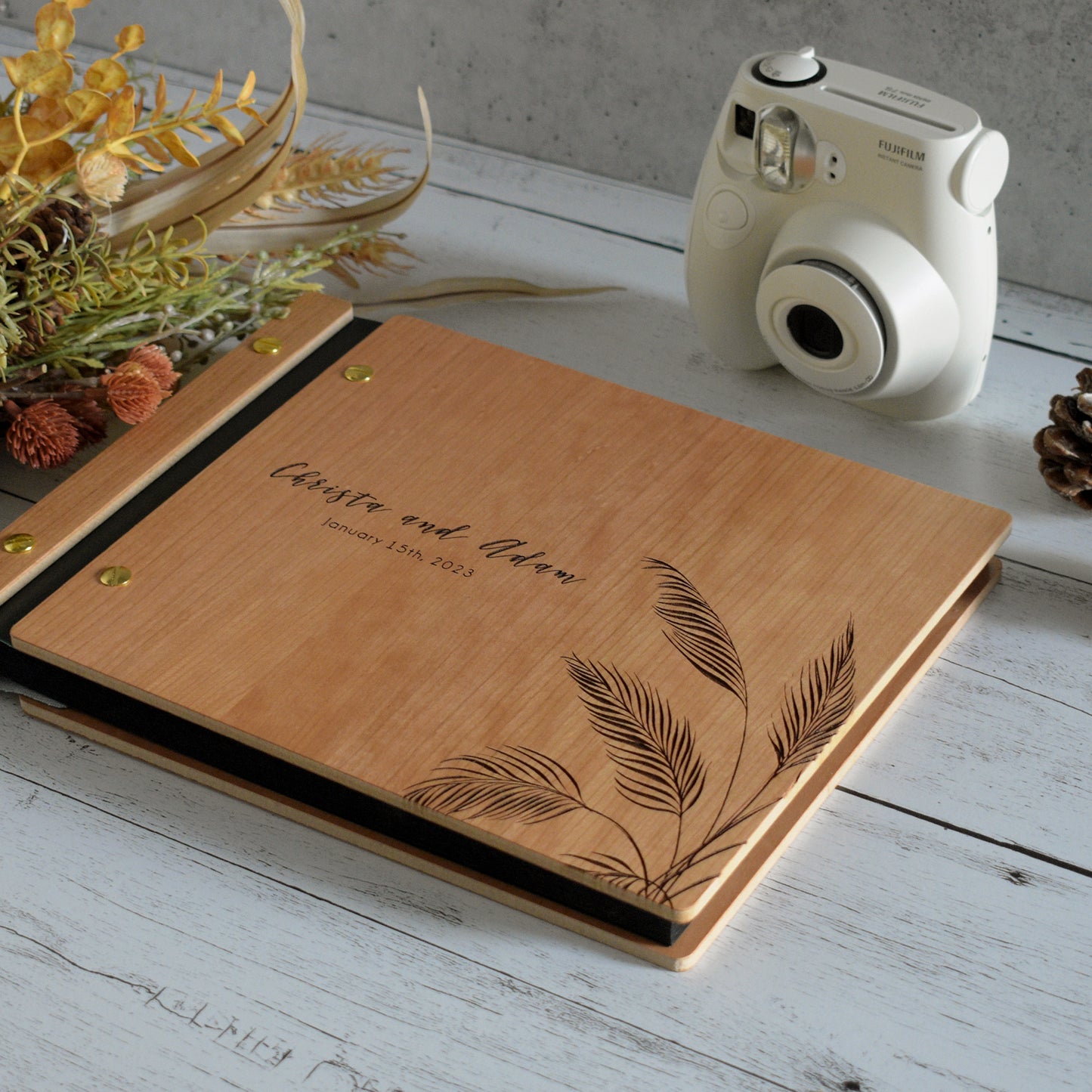 An 8.5x11" guest book lies on a table. Made of cherry wood, black vegan leather binding, and copper hardware. The front cover reads “Christina and Adam, January 15th, 2023.” 