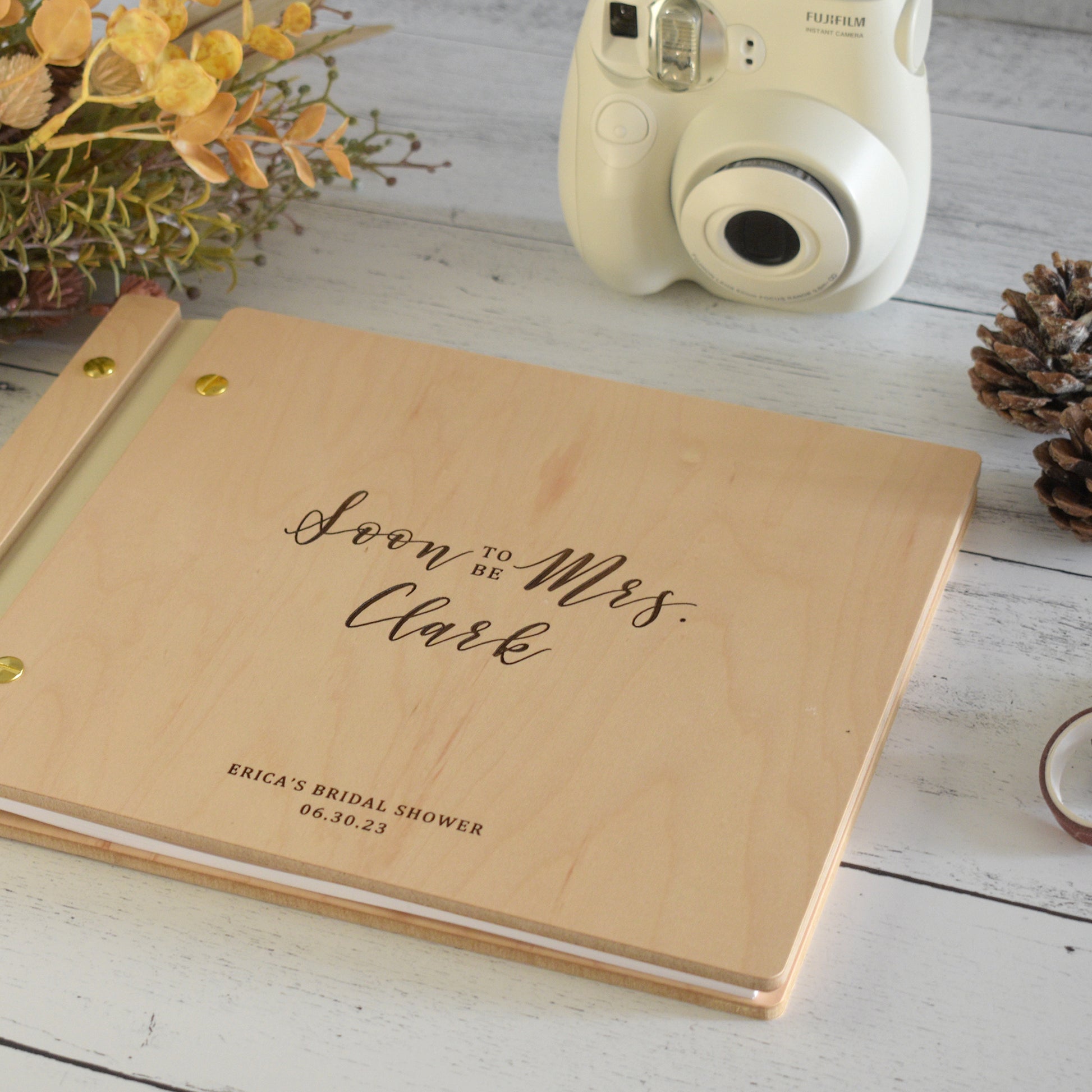 An 8.5x11" wedding guest book lies on a table. Made of cherry or maple wood, vegan leather binding, and aluminum hardware. The front cover includes an engraved design with personalization.