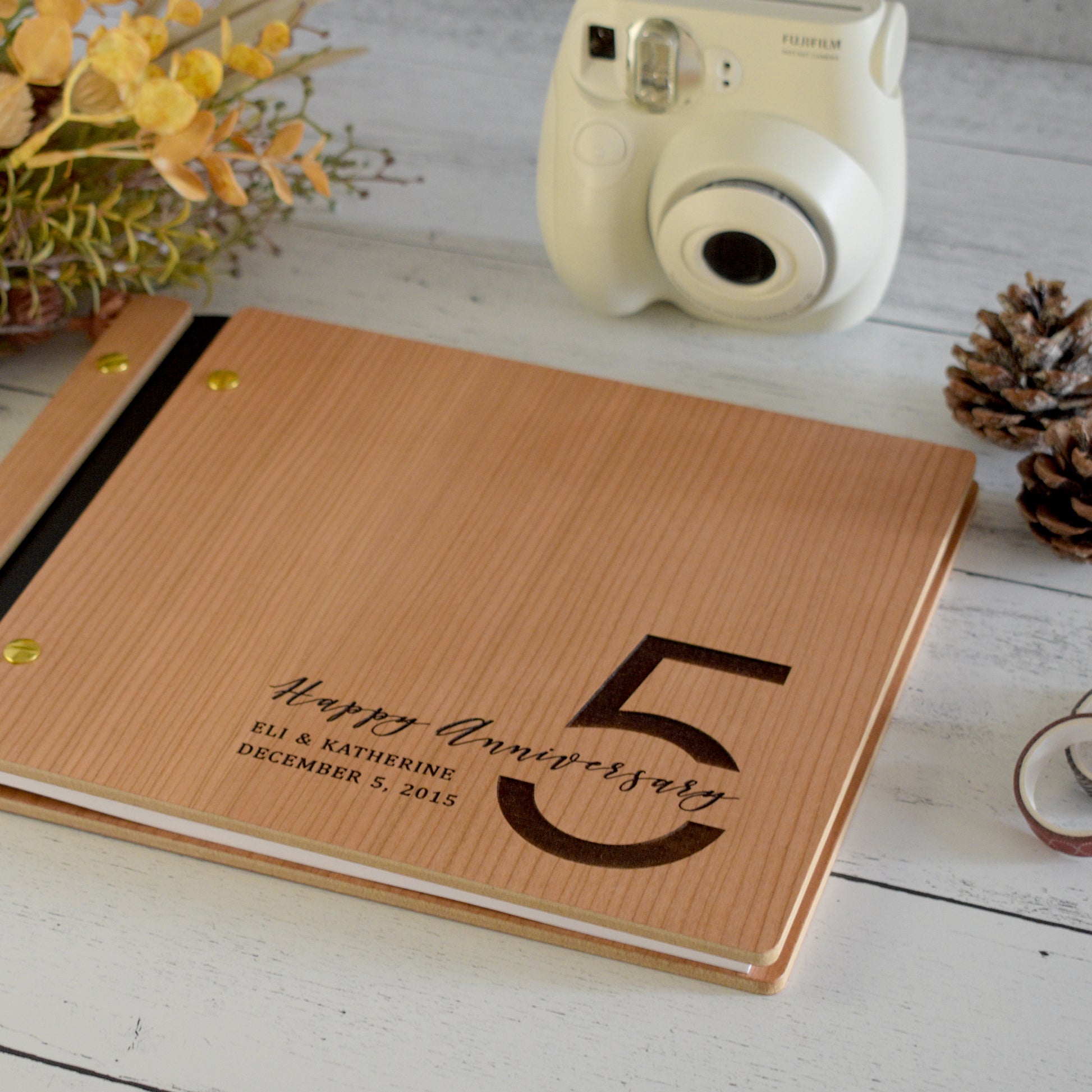 An 8.5x11" guest book lies on a table. Made of cherry wood, black vegan leather binding, and gold hardware. The front cover reads “Happy Anniversary, Eli & Katherine, December 5th, 2015."