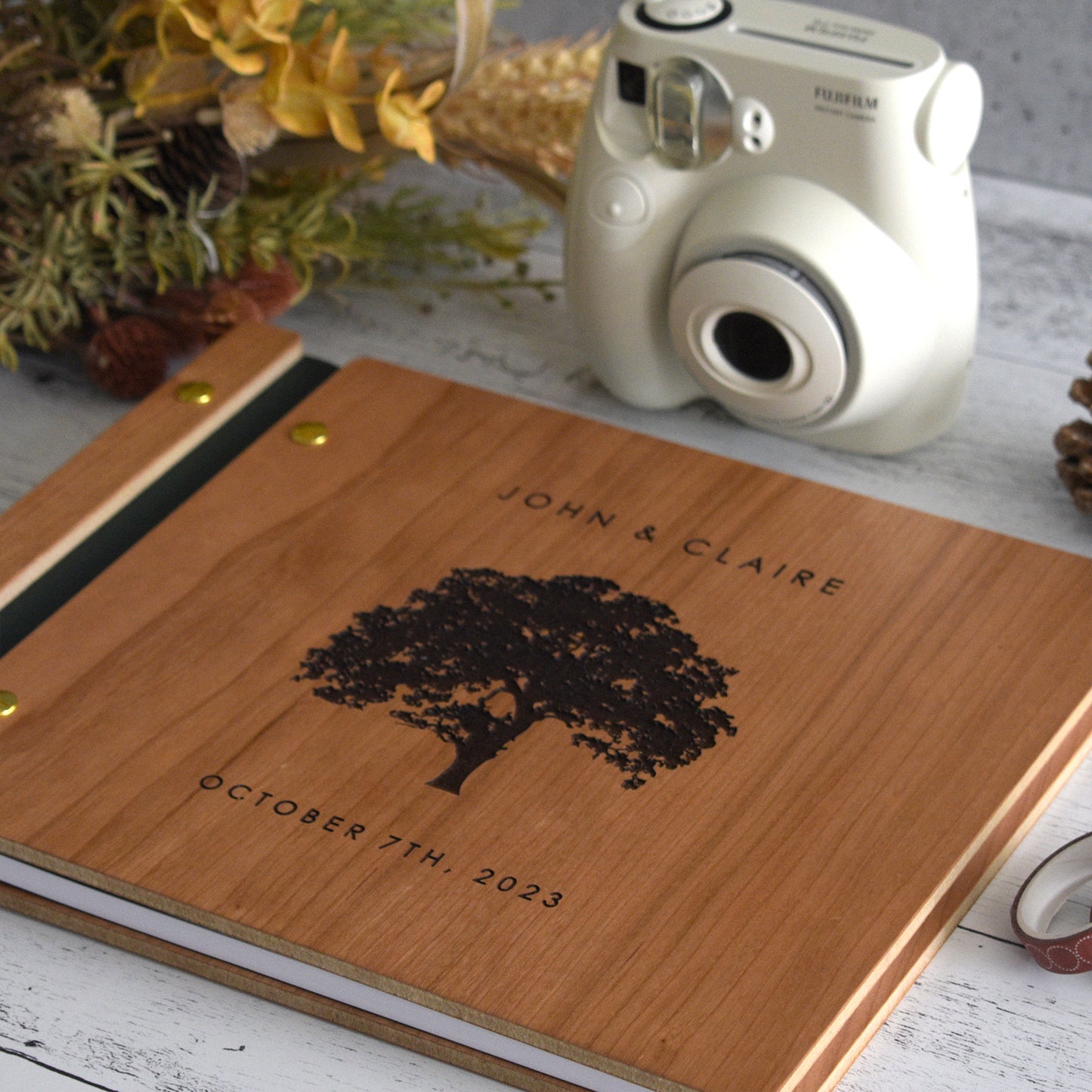 An 8.5x11" guest book lies on a table. Made of cherry wood, black vegan leather binding, and copper hardware. The front cover includes an engraved design with personalized names.
