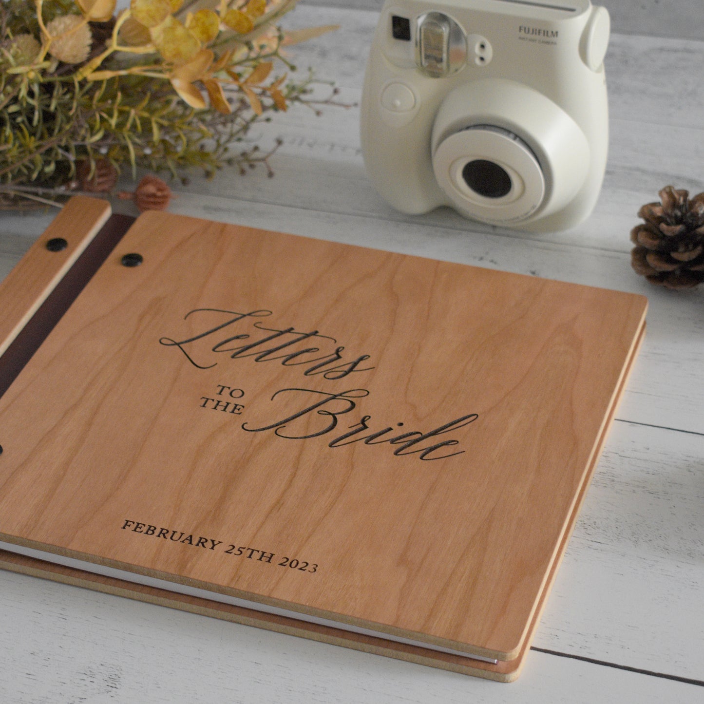 An 8.5x11" guest book lies on a table. Made of cherry wood, black vegan leather binding, and black hardware. The front cover includes an engraved design with personalization.