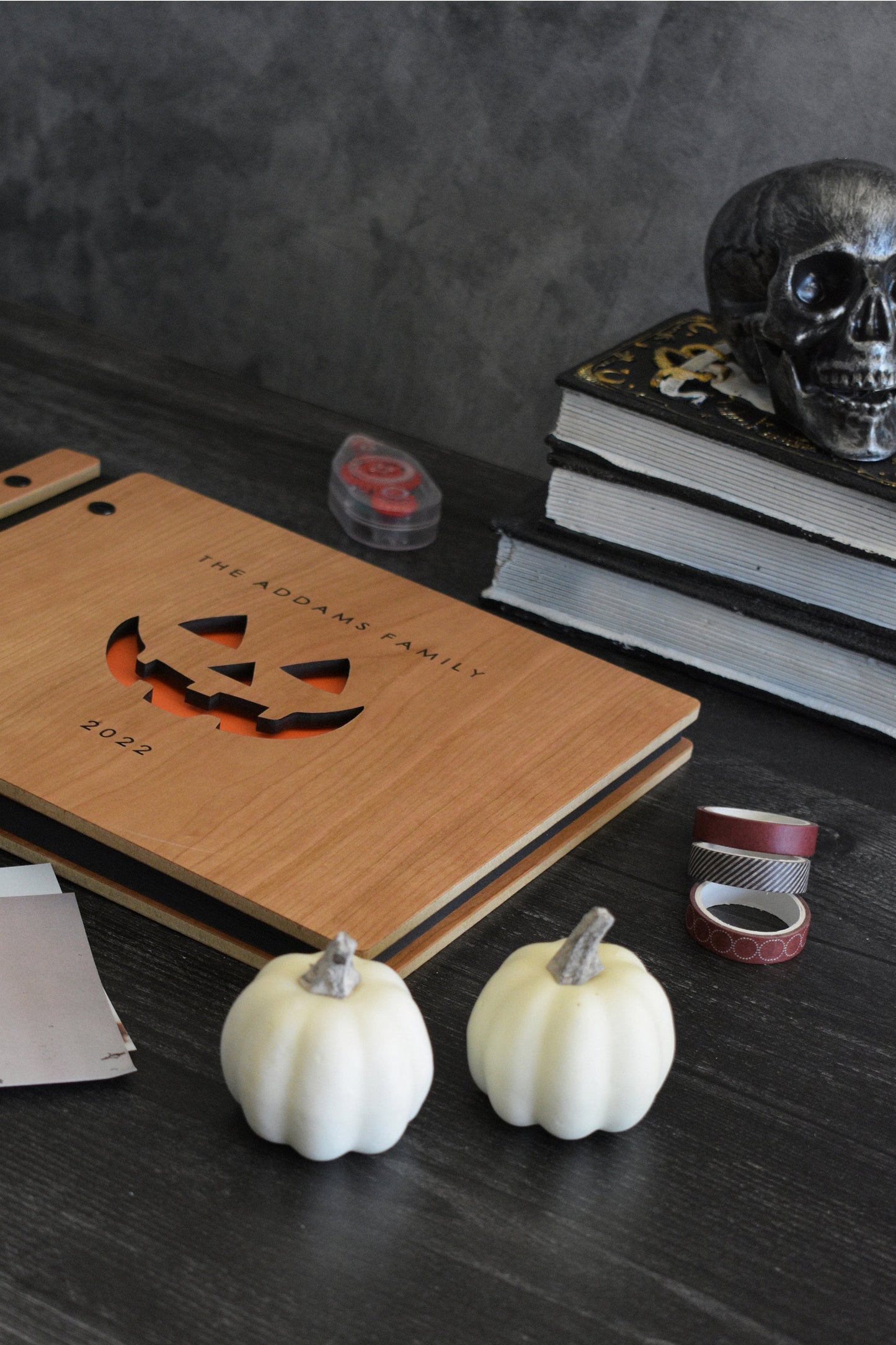 An 8.5x11" guest book lies on a table. Made of cherry wood, black vegan leather binding, and black hardware. The front cover reads The Addams Family, 2022 with an engraved pumpkin in the center.
